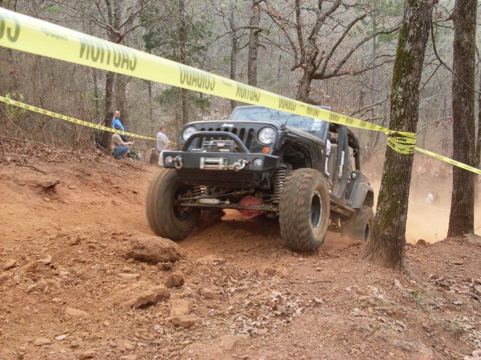 Black Jeep Wrangler navigating a muddy off-road course under caution tape