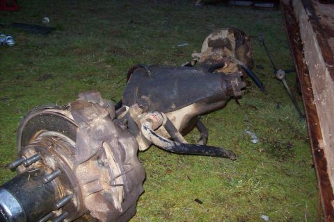 1995 Ford Bronco - A front axle assembly, likely from a truck or SUV, is shown disassembled and resting on a grassy surface.