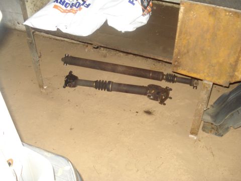 1991 Ford Bronco - Two driveshafts, likely from a vehicle, are shown on a concrete floor with a white bag and yellow metal in the background.
