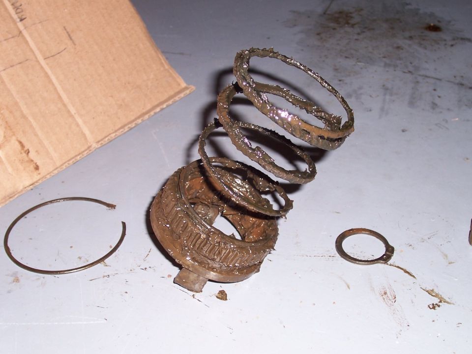 Greasy metal rings and a gear-like part are spread out on a surface next to a piece of cardboard