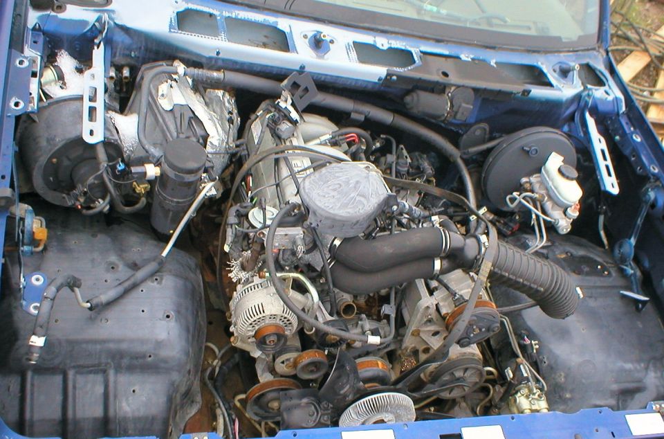 Engine bay of a blue vehicle with V8 swapped in, alternator and intake visible amid wiring