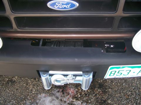 1993 Ford Bronco - Close-up of a winch mounted in a black front bumper on a brown Ford truck, with the wire rope spooled on the drum, a chrome hook and polish…