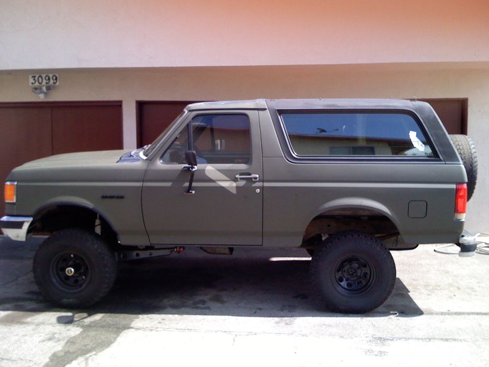 Olive green lifted Ford Bronco SUV parked in front of a garage