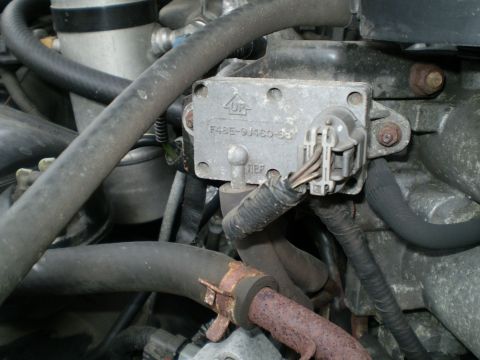 1996 Ford Bronco - Close-up of an engine-bay component cast with the part number 'F48E-9J460-BB' and an 'UP' arrow marking, with a gray electrical connector p…