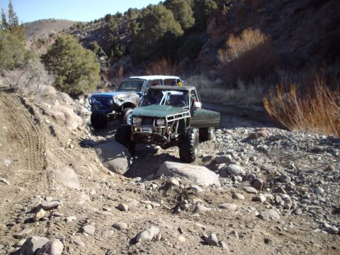 1982 Toyota 4Runner - Two heavily modified trucks tackle a challenging, rocky off-road path.