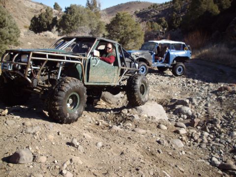 1982 Toyota 4Runner - Two modified off-road vehicles navigate a rocky, mountainous trail under a clear sky.