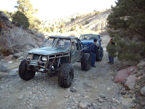 1982 Toyota 4Runner - Two off-road vehicles, a custom buggy and a pickup truck, are stopped on a gravel path in a dry, hilly landscape.