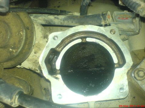 1992 Ford Crown Victoria - Overhead close-up of a throttle body mounted on the engine with the intake ducting removed, revealing a wet, oily black carbon film on the…