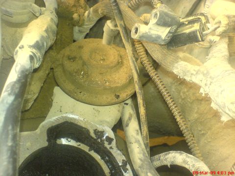 1992 Ford Crown Victoria - Dusty engine-bay close-up of a round vacuum-diaphragm EGR valve mounted on the intake, surrounded by grime-covered hoses, a spring-wound li…