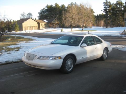 1998 Lincoln Mark VIII - A white coupe sits in a driveway with snow on the ground and trees in the background.