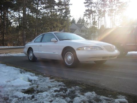 1998 Lincoln Mark VIII - A white coupe is parked on a road with snow on the side, with a dark vehicle partially visible to the right.