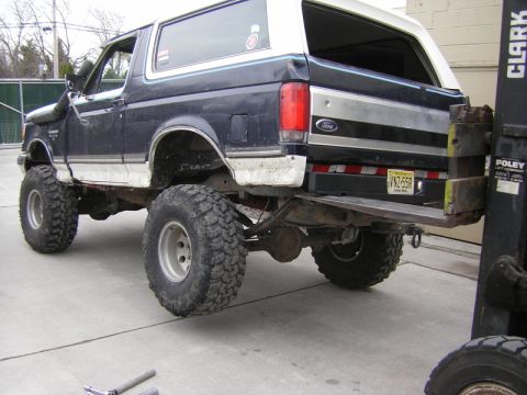 1989 Ford Bronco - A modified Ford Bronco with off-road tires and a snorkel is viewed from the rear, with a forklift nearby.