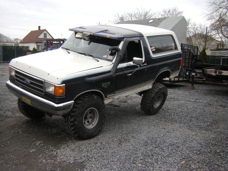 Lifted blue and white Ford Bronco on gravel with snorkel, light bar and mud-terrain tires