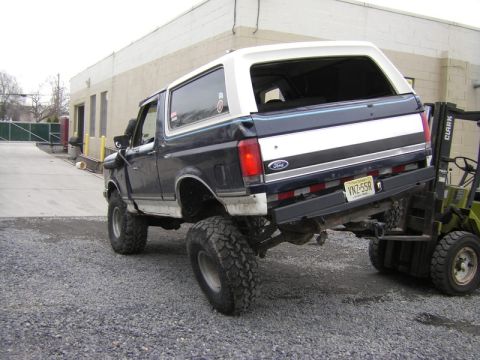 1989 Ford Bronco - Forklift lifting a modified 1989 Ford Bronco by its rear bumper.