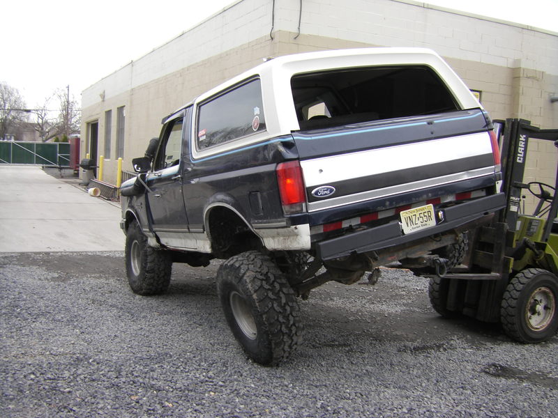 Lifted blue and white Ford Bronco lifted by a Clark forklift outside a shop building