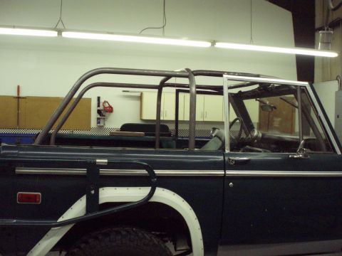 1977 Ford Bronco - The interior of a dark green Ford Bronco is visible, a custom roll cage and fender flares.