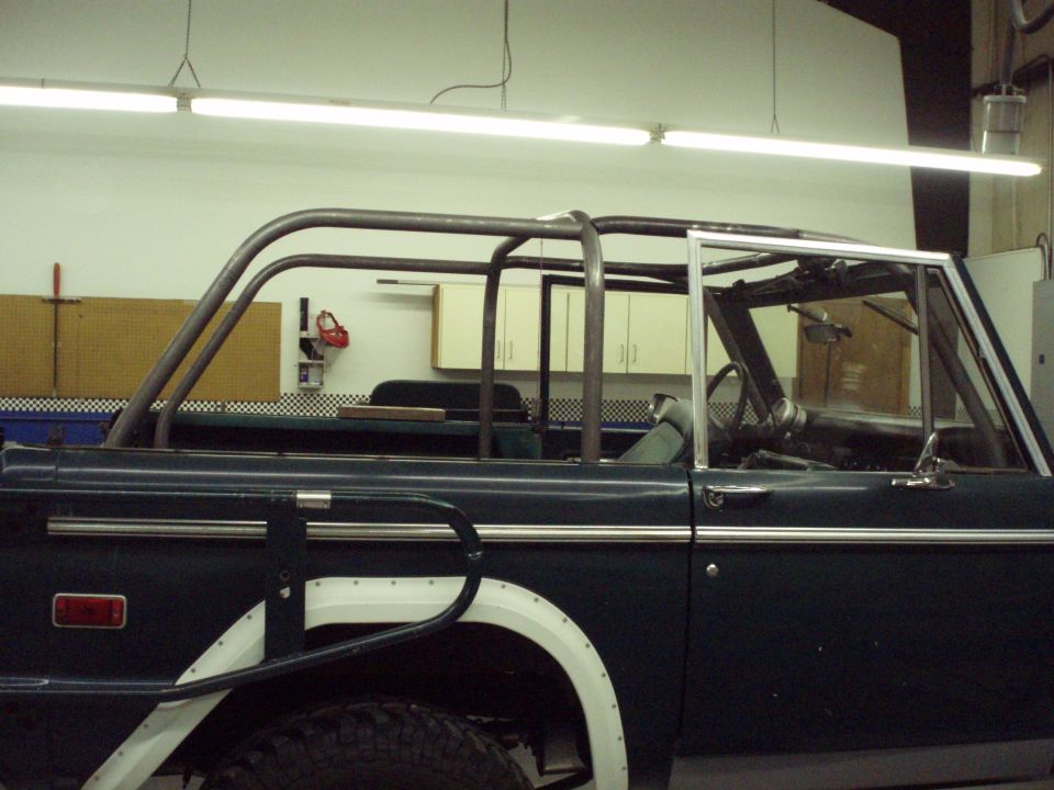 dark green Ford Bronco with custom roll cage, side view showing interior and fender flare