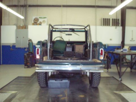 1977 Ford Bronco - Rear view of a 1977 Ford Bronco with an aftermarket roll cage, parked inside a workshop.
