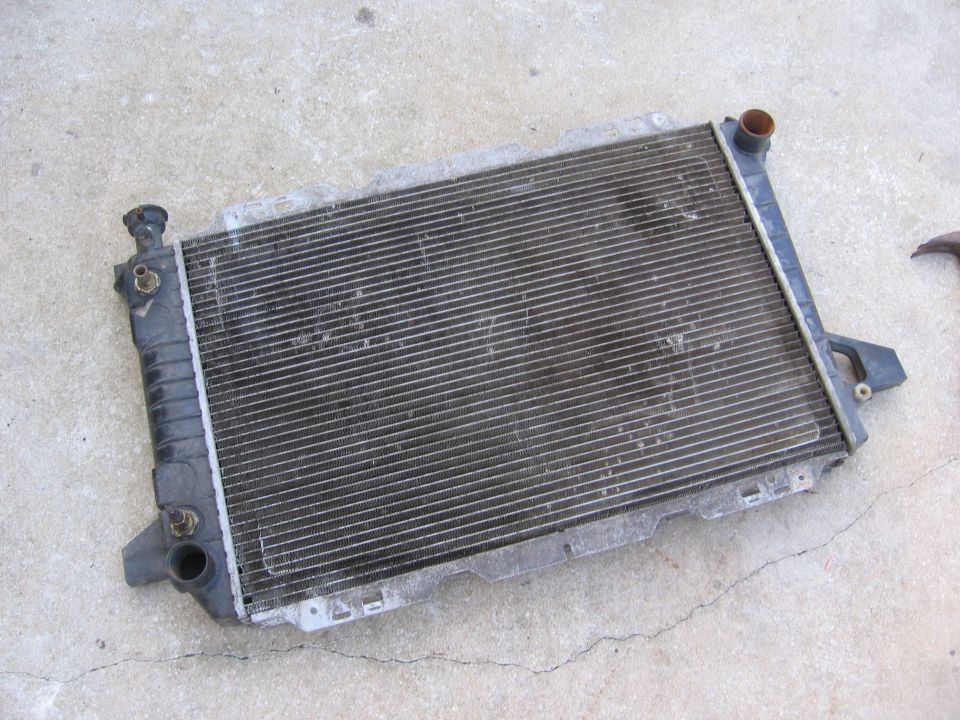 Used aluminum and plastic radiator lying on concrete, with filler neck and hose connections visible.