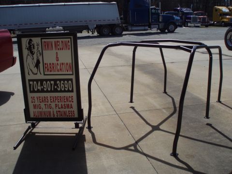 1977 Ford Bronco - A custom roll cage is shown next to a business sign advertising welding and fabrication services.