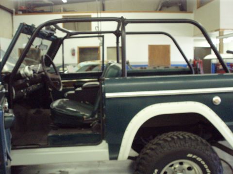 1977 Ford Bronco - The side view of a dark green 1977 Ford Bronco reveals its interior, roll cage, and white fender flares.