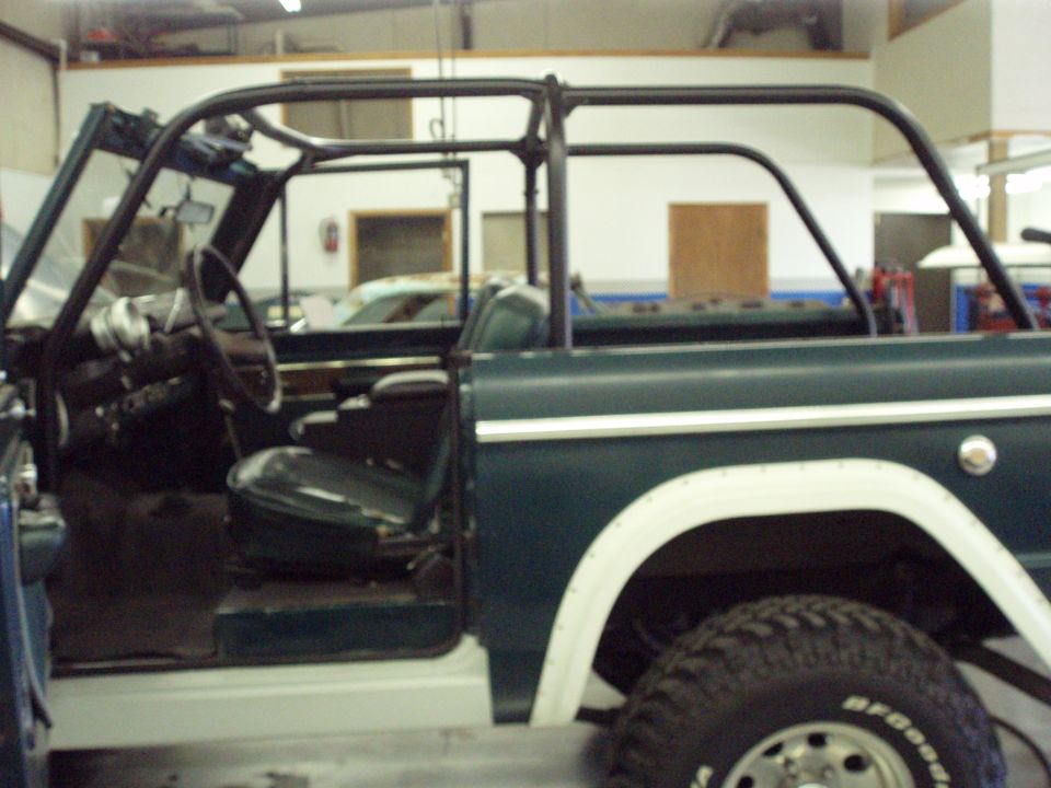 Dark green 1977 Ford Bronco interior and side profile, with roll cage and white fender flares