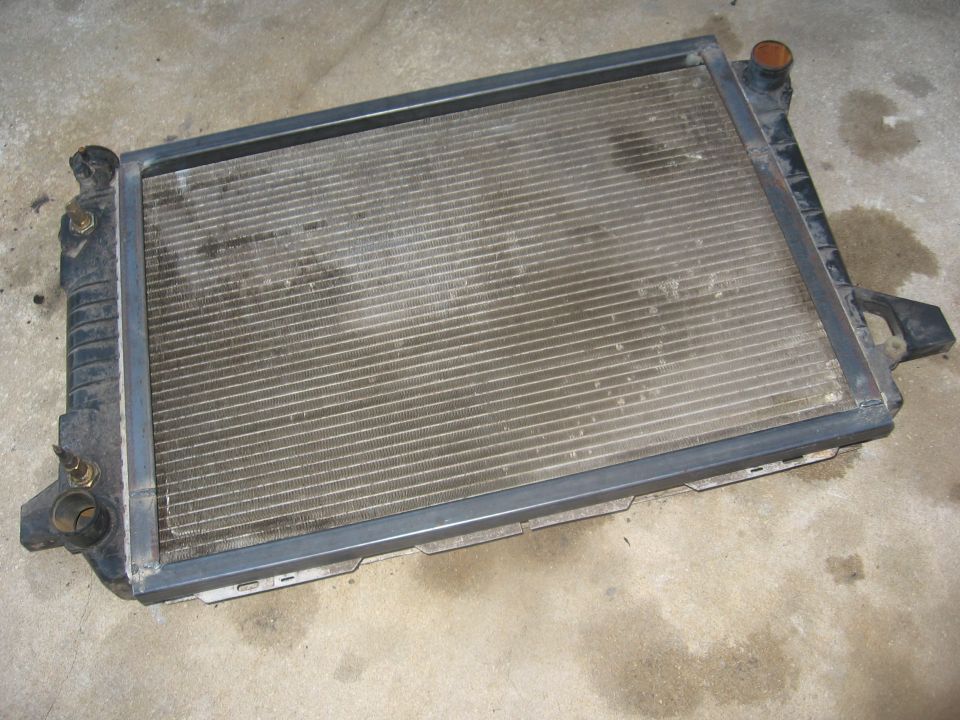 Removed automotive radiator with black plastic tanks lying on a concrete garage floor