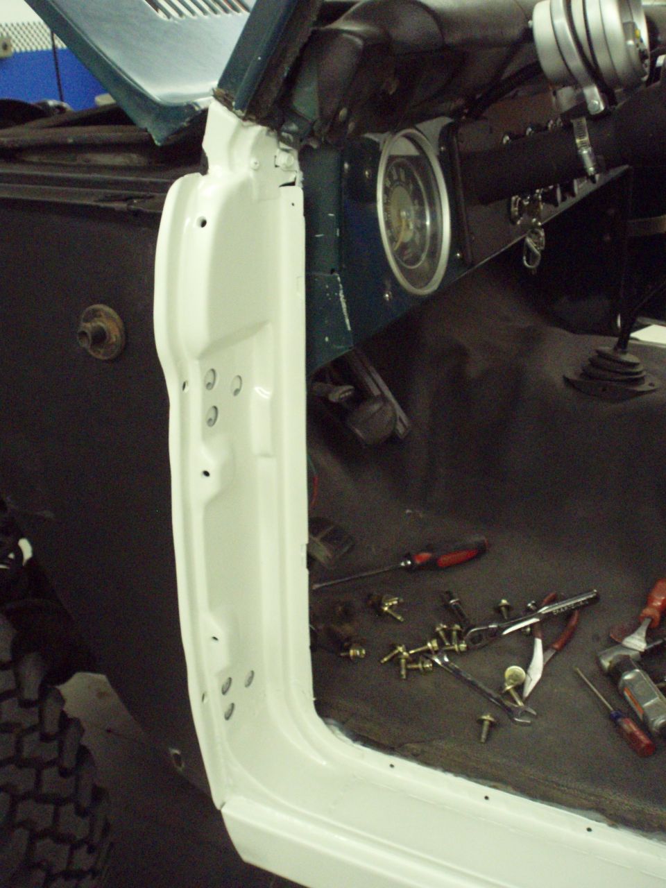 Interior of a vehicle with door removed, showing dashboard, steering column, and floor with tools and hardware scattered