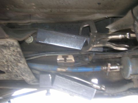 1996 Ford Bronco - A close-up view of a vehicle's undercarriage shows a metal part secured with vice grips, alongside fuel lines and a filter.