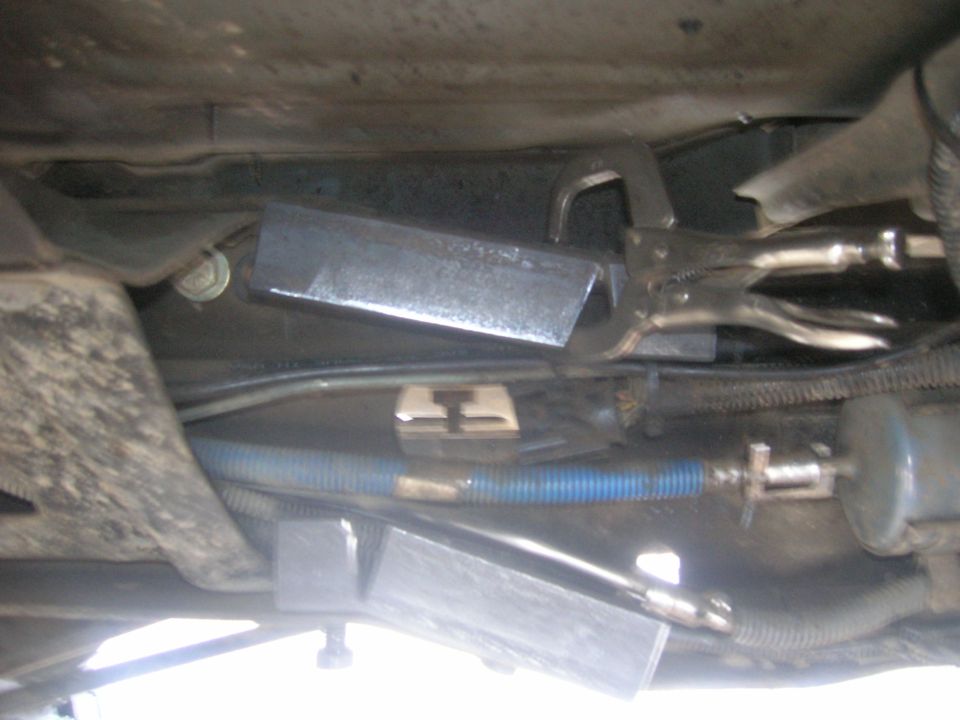 Underbody part held by vice grips, with blue hose and fuel filter visible