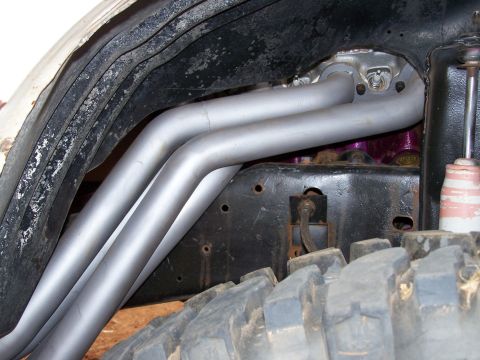 1995 Ford Bronco - This image shows the exhaust headers and part of the suspension system of a vehicle, with a large off-road tire in the foreground.