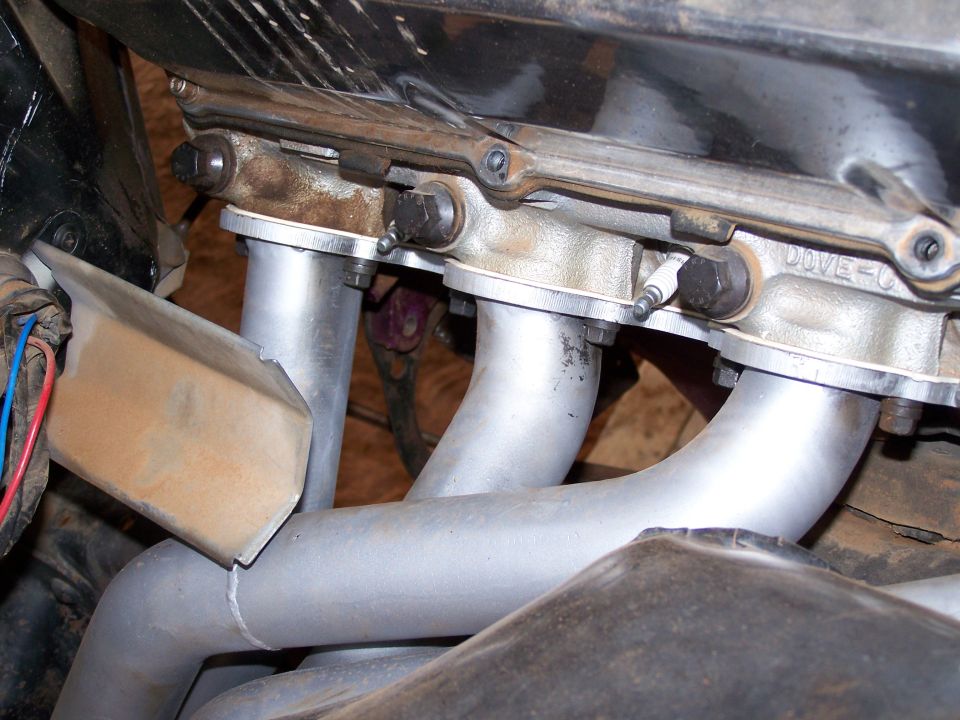 Close-up of exhaust manifold pipes connected to engine block with bolts. 'DOVE-C' is visible