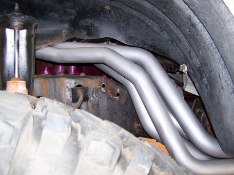 1995 Ford Bronco - Close-up view of exhaust headers and suspension parts under a vehicle, with a tire in the foreground.