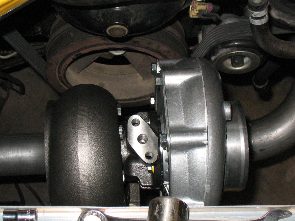 Turbocharger mounted to engine block with exhaust manifold and pulley system visible