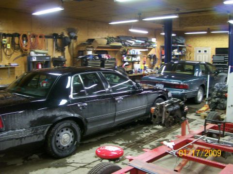 1995 Mercury Grand Marquis - Two sedans are parked in a garage, with a disassembled engine nearby.