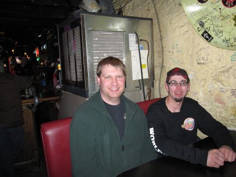 1992 Ford Bronco - Two men are seated at a table in a bar, with a large cooler and graffiti-covered wall behind them.