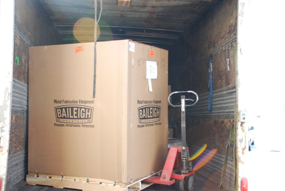 Pallet jack next to a large cardboard box labeled 'Baileigh Industrial' inside a truck trailer