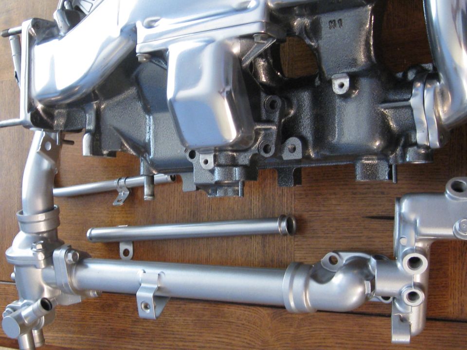 engine intake manifold and some metal pipes laid out on a wooden surface