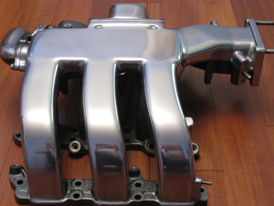 Polished aluminum intake manifold with four runners, mounted on a wooden surface