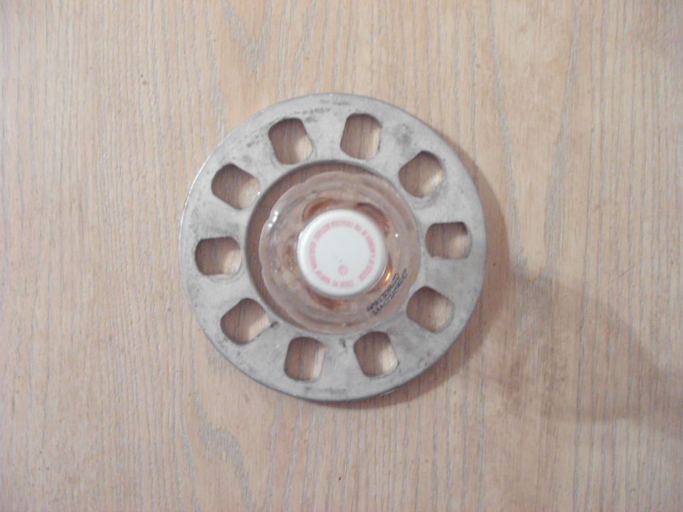Aluminum wheel spacer with a clear plastic cap and white lid on a wooden surface