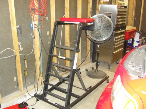 2007 Ford Mustang - A red car is partially visible next to a rolling ladder lift and a large fan in a garage.