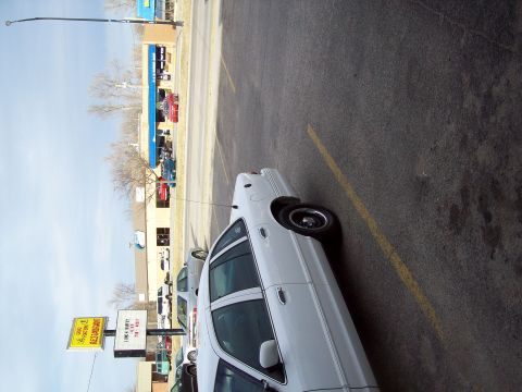 2000 Mercury Grand Marquis - A white sedan is parked in a lot with other vehicles and a building visible in the background.