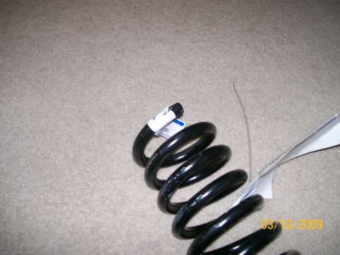 1995 Mercury Grand Marquis - A single black coil spring is shown lying on a carpeted surface with attached tags and a date stamp.