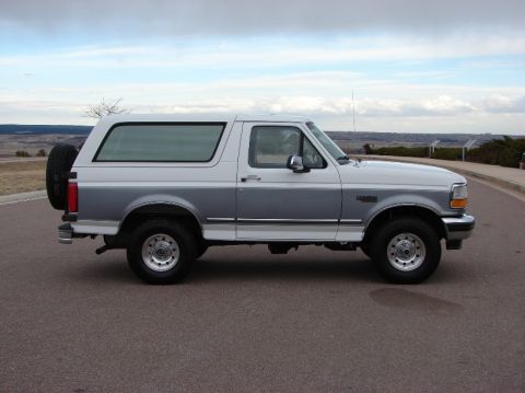 1995 Ford Bronco - This two-tone Ford Bronco is shown from the side, parked on a road with a scenic overlook.