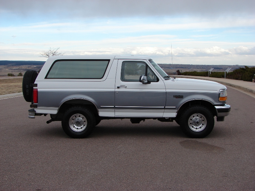 Side view of a two-tone silver and white Ford Bronco parked on asphalt with a landscape in the background