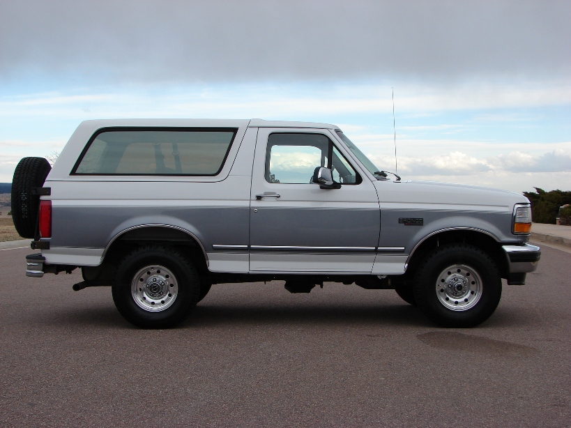 Two-tone silver and white Ford Bronco with a spare tire mounted on the rear, seen from the side