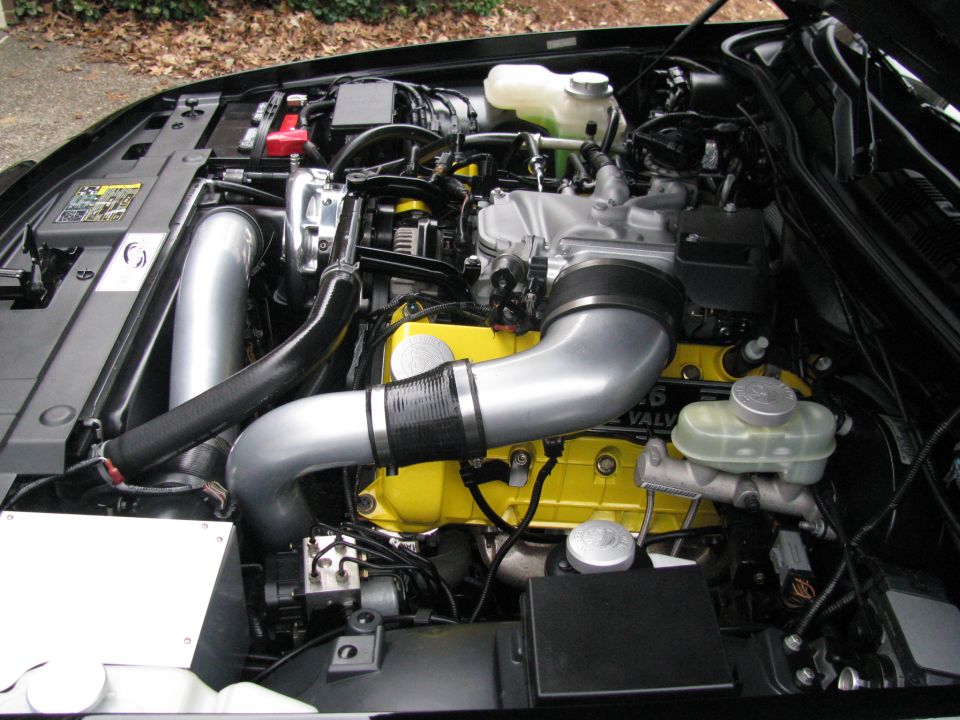 Engine bay with yellow valve covers, large intake piping, and turbocharger components. Text on valve cover reads '4.6L 32 VALVE'