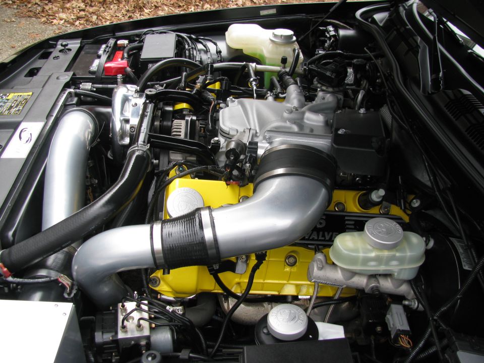 Engine bay with yellow valve covers and silver intake piping. Supermotors.net logo visible
