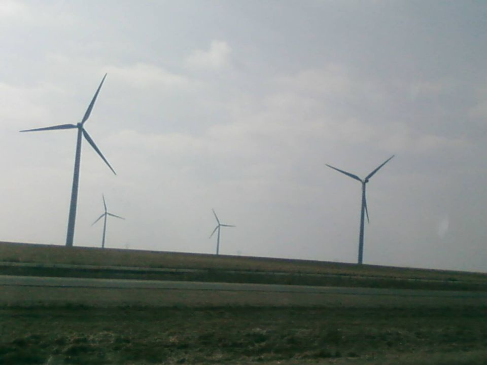 Several wind turbines stand on a grassy hill under a cloudy sky
