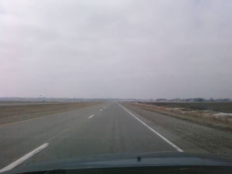 1985 Ford LTD Crown Victoria - A long, straight highway stretches into the distance under an overcast sky.